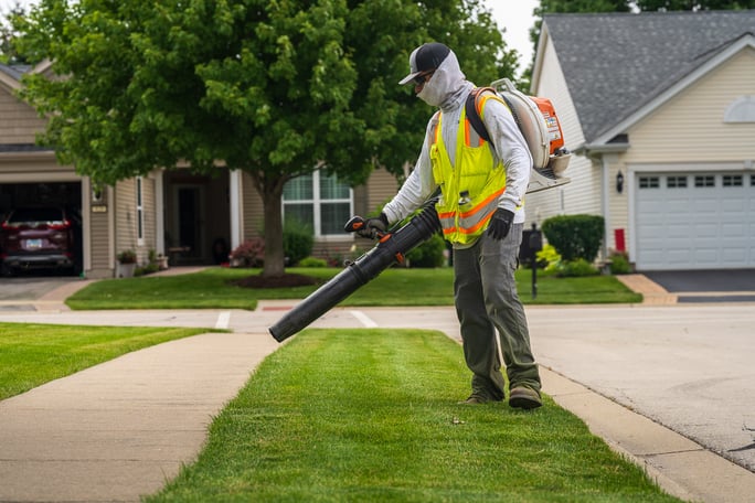 landscape maintenance team member blowing grass clippings off a sidewalk