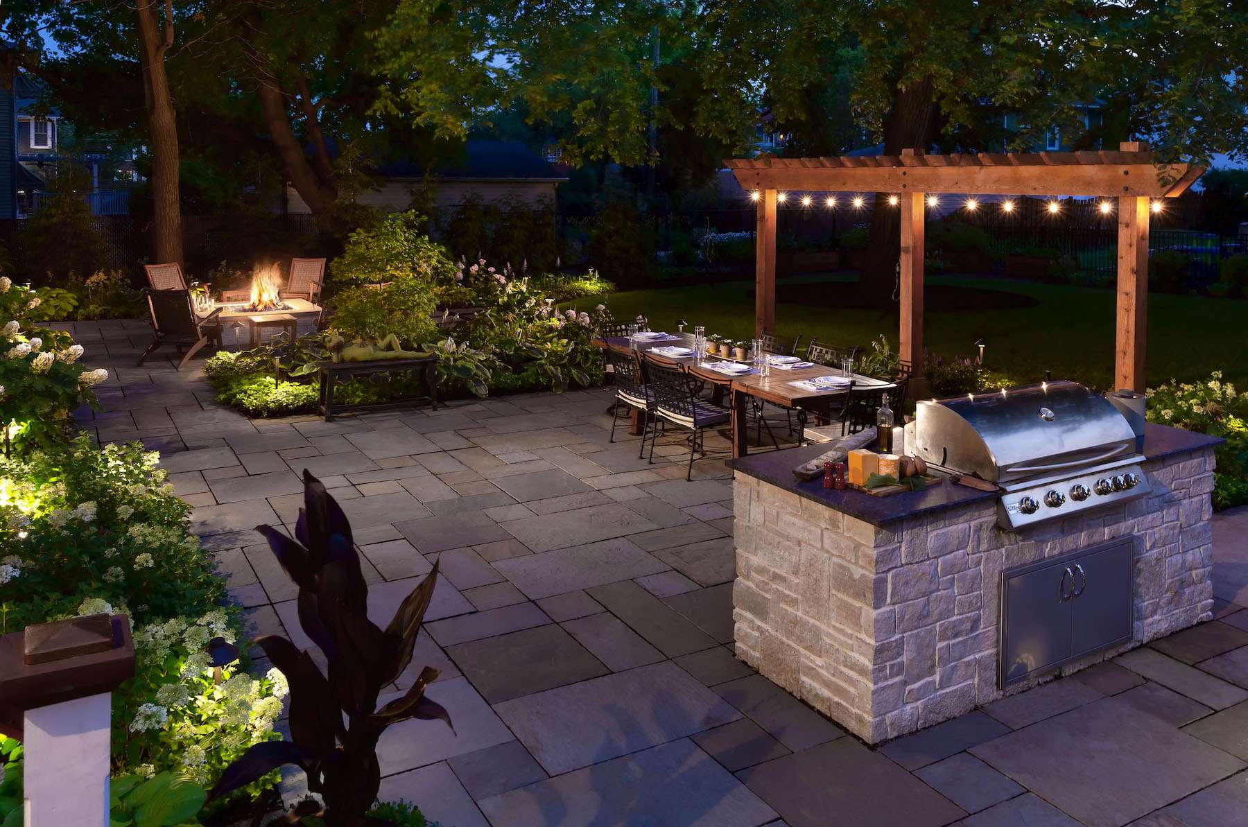 landscape lighting in flower beds and on pergola with outdoor kitchen firepit and patio