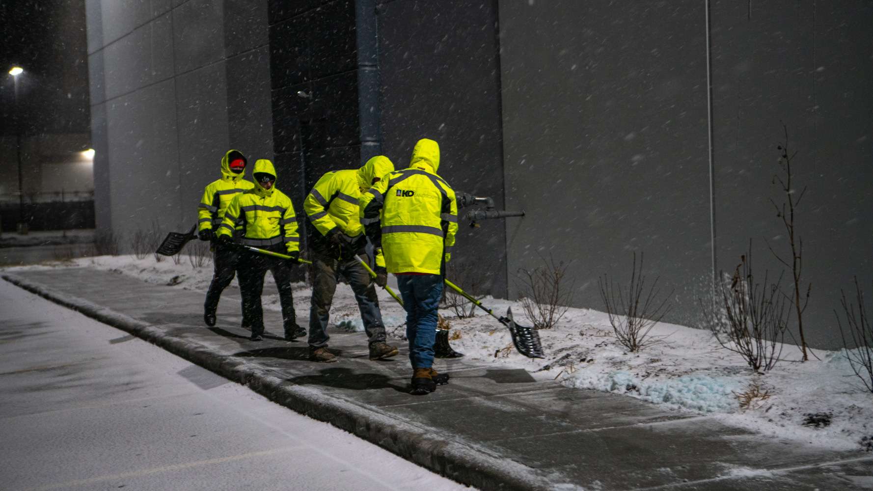 commercial snow removal technicians shoveling a sidewalk at a commercial warehouse