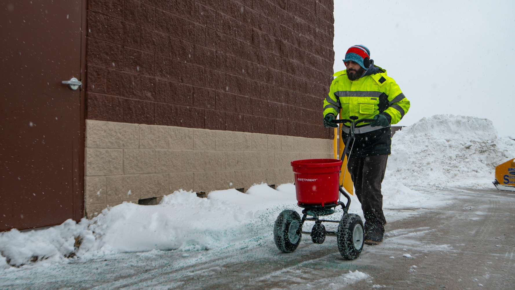 commercial snow removal technician spreading icemelt on a sidewalk