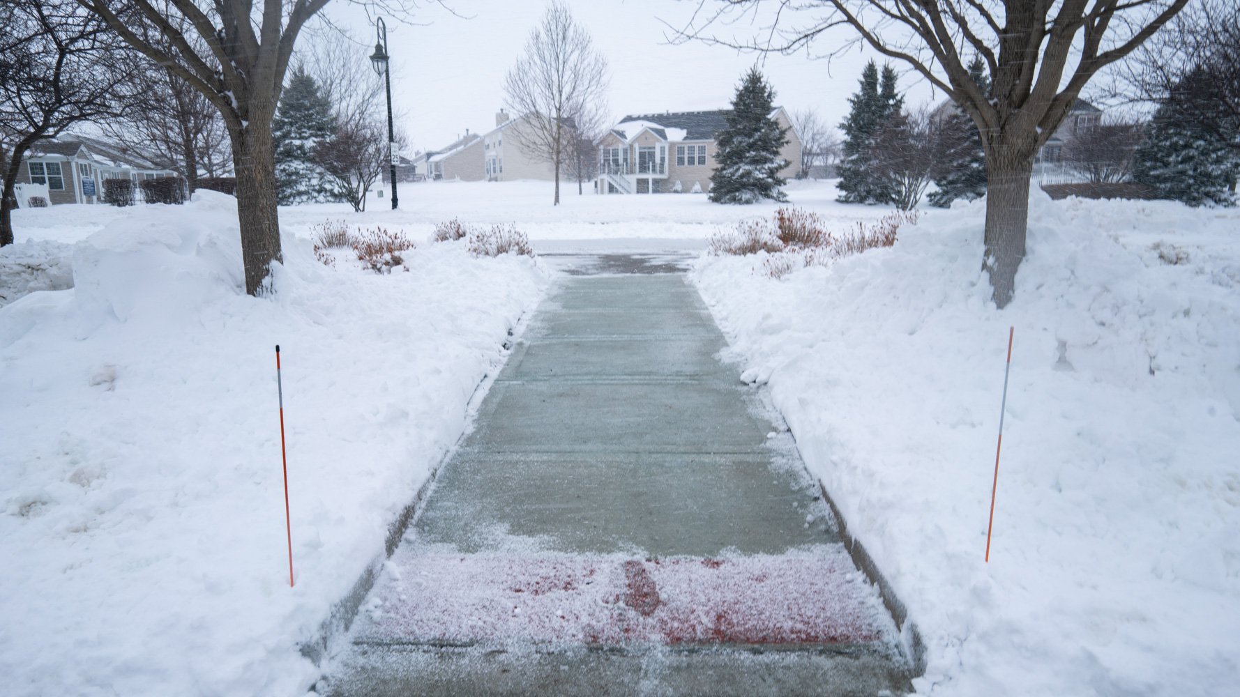 cleared sidewalk at an HOA with snow stakes marking edges of the walkway in the snow