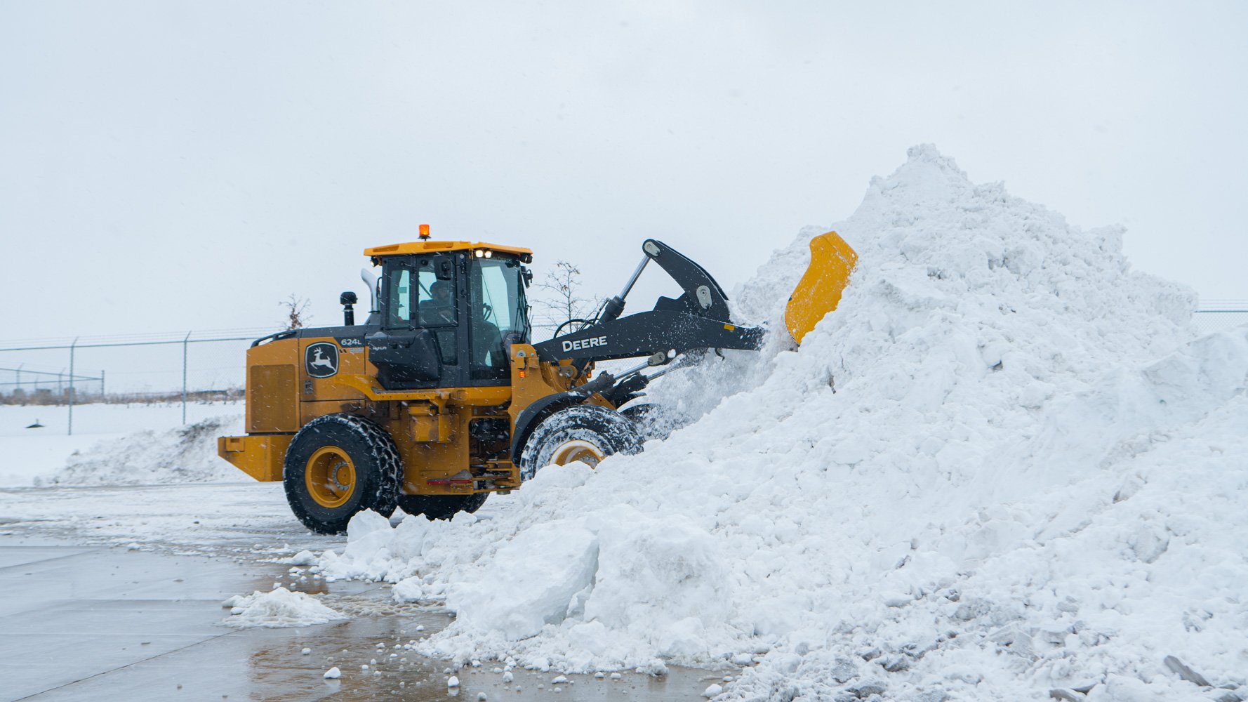 commercial snow removal plow loader moving a large pile of snow at an industrial warehouse parking lot