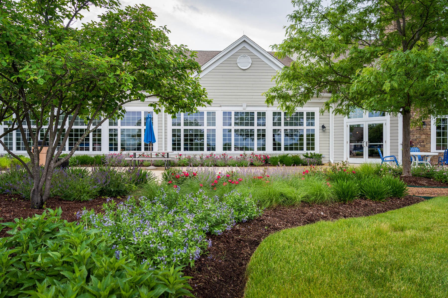 landscape planting bed in front of an HOA common building with shrubs perennials and ornamental trees