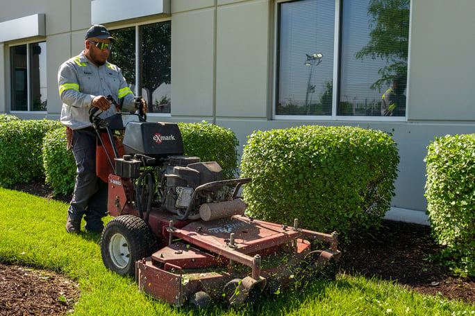 commercial maintenance technician mowing warehouse lawn