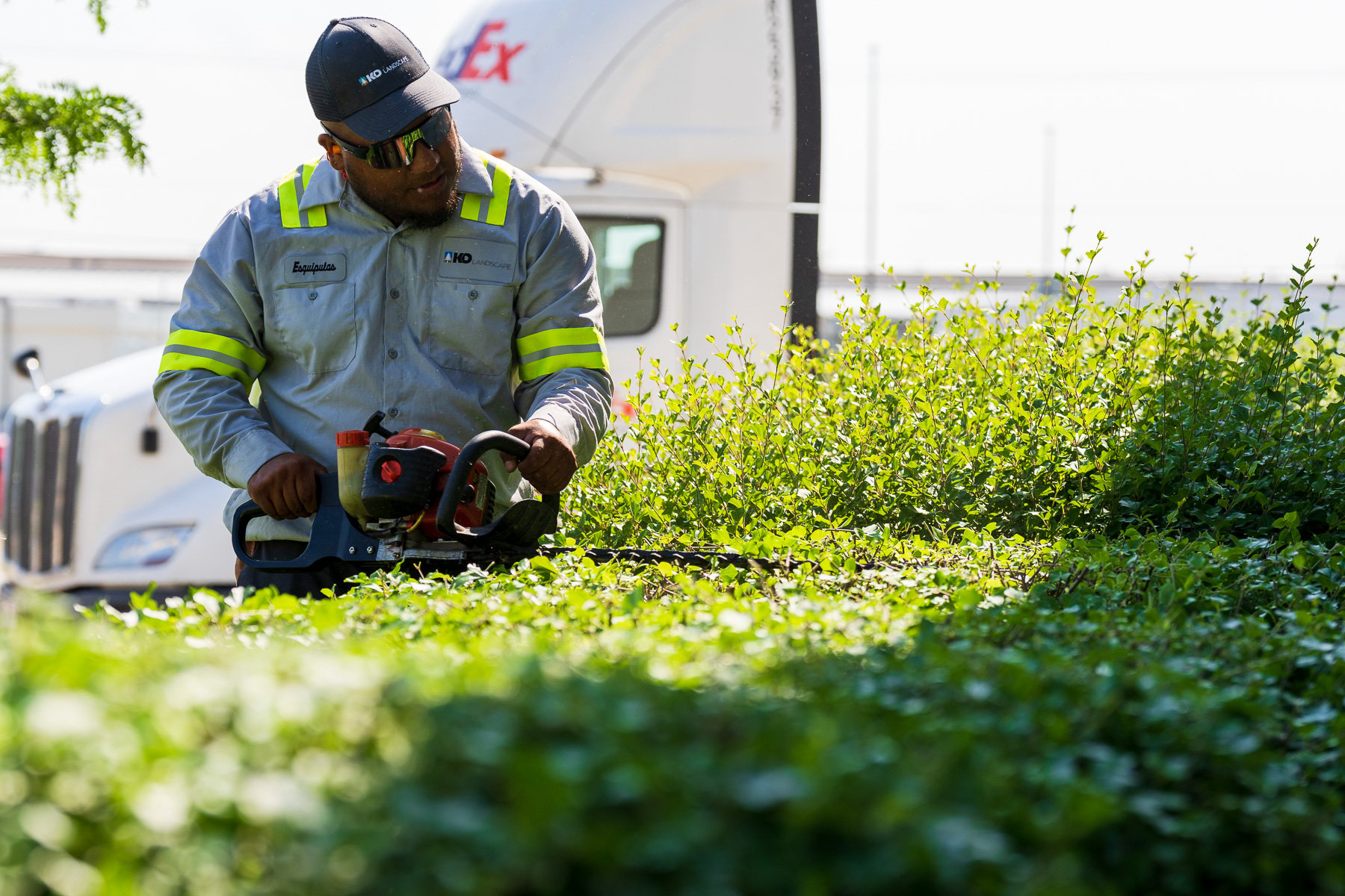 commercial maintenance technician shearing a hedge in front of a commercial warehouse