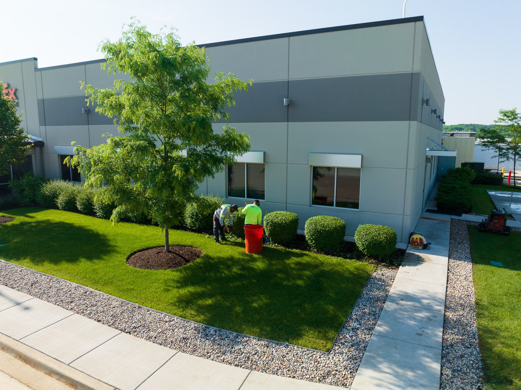commercial landscape maintenance crew pruning shrubs and cleaning planting beds at a commercial warehouse